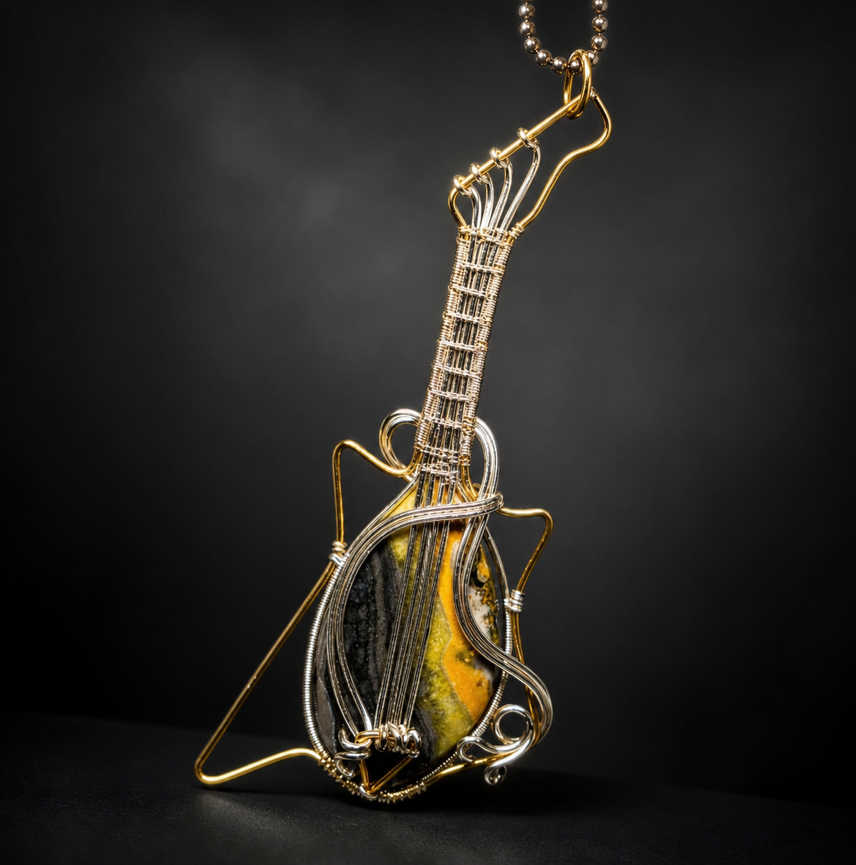 A detailed handcrafted wire-wrapped electric guitar pendant featuring a teardrop-shaped yellow and black bumblebee jasper gemstone body and woven metal strings