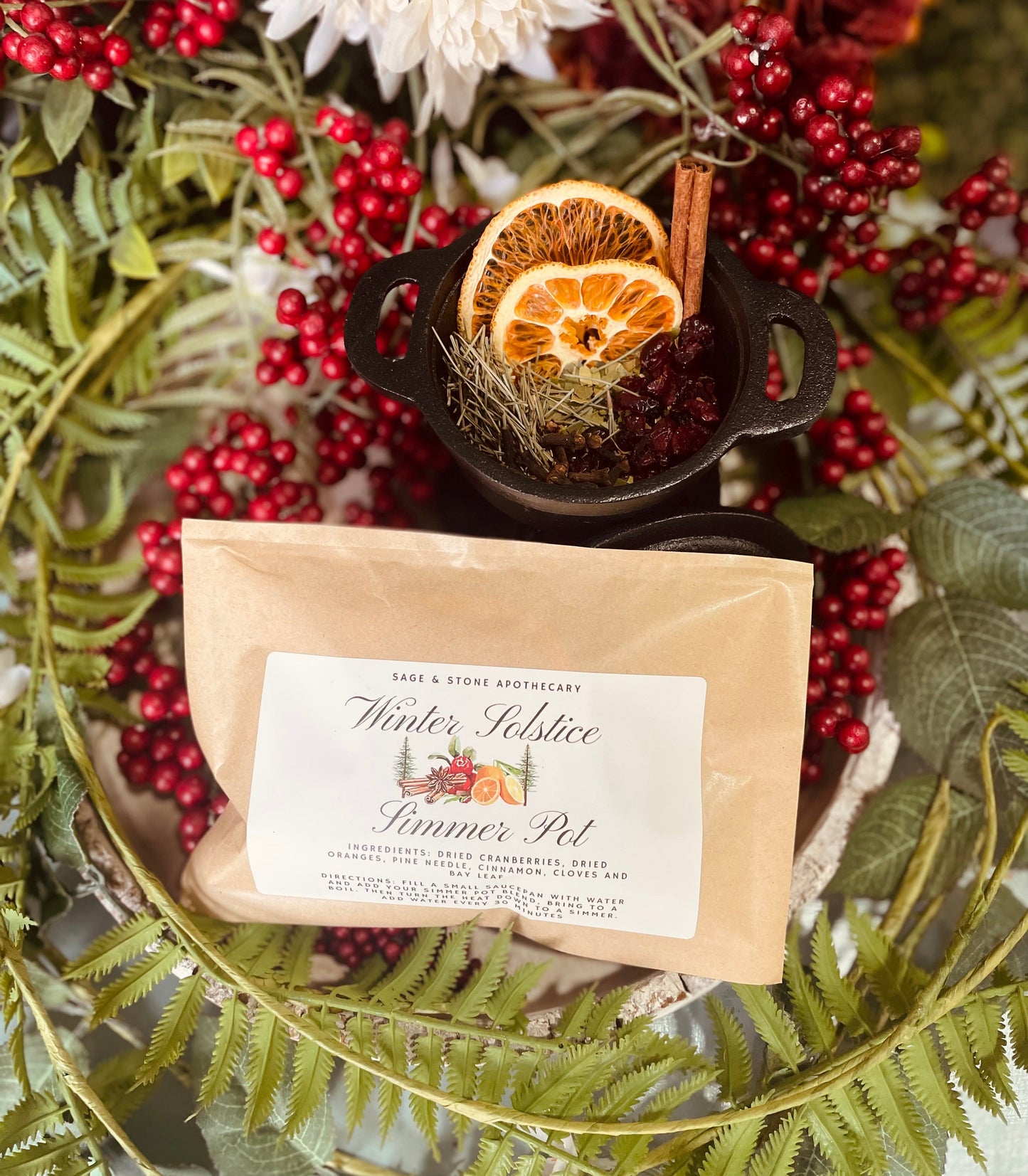 A clean side-by-side view of the Winter Solstice Simmer Pot pouch packaging alongside a prepared aromatic holiday potpourri arrangement for online store display.