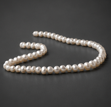 A single full 15-inch strand of cream baroque large hole freshwater pearls laid out in a wavy display on a clean white background.