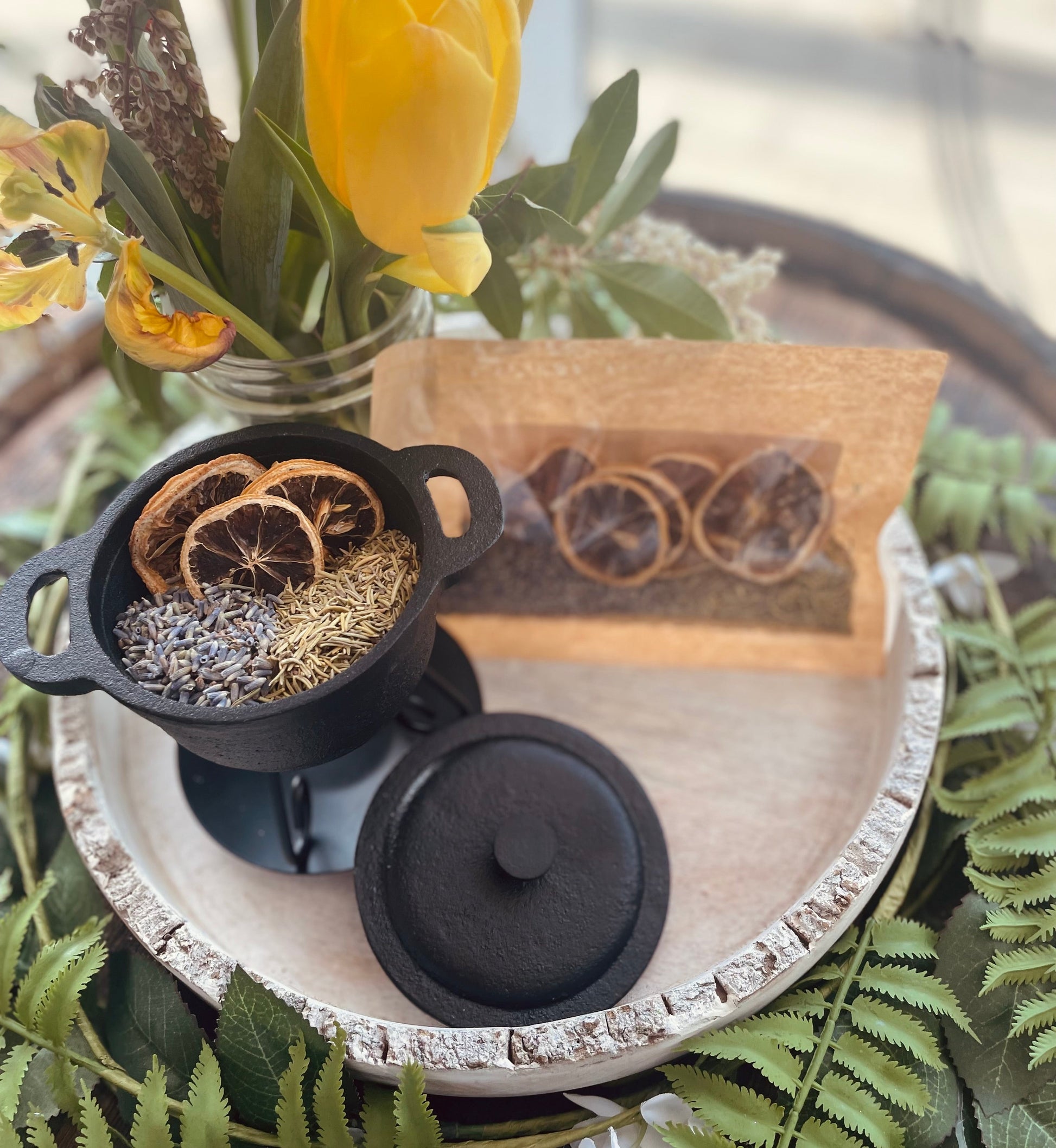 High-angle shot showing the botanical simmer pot kit with its craft paper bag pouch and small black pot arranged on a rustic white decorative tray.