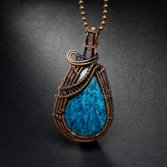 A detailed handcrafted antiqued copper wire-wrapped pendant showcasing a textured teardrop-shaped deep blue apatite gemstone
