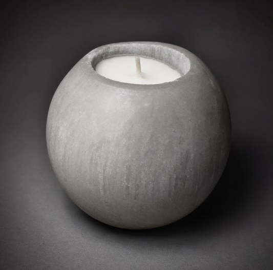 A hand-carved spherical white selenite crystal tealight candle holder with a lit wax candle inside, showing the soft glow through the natural stone fibers against a dark grey background.