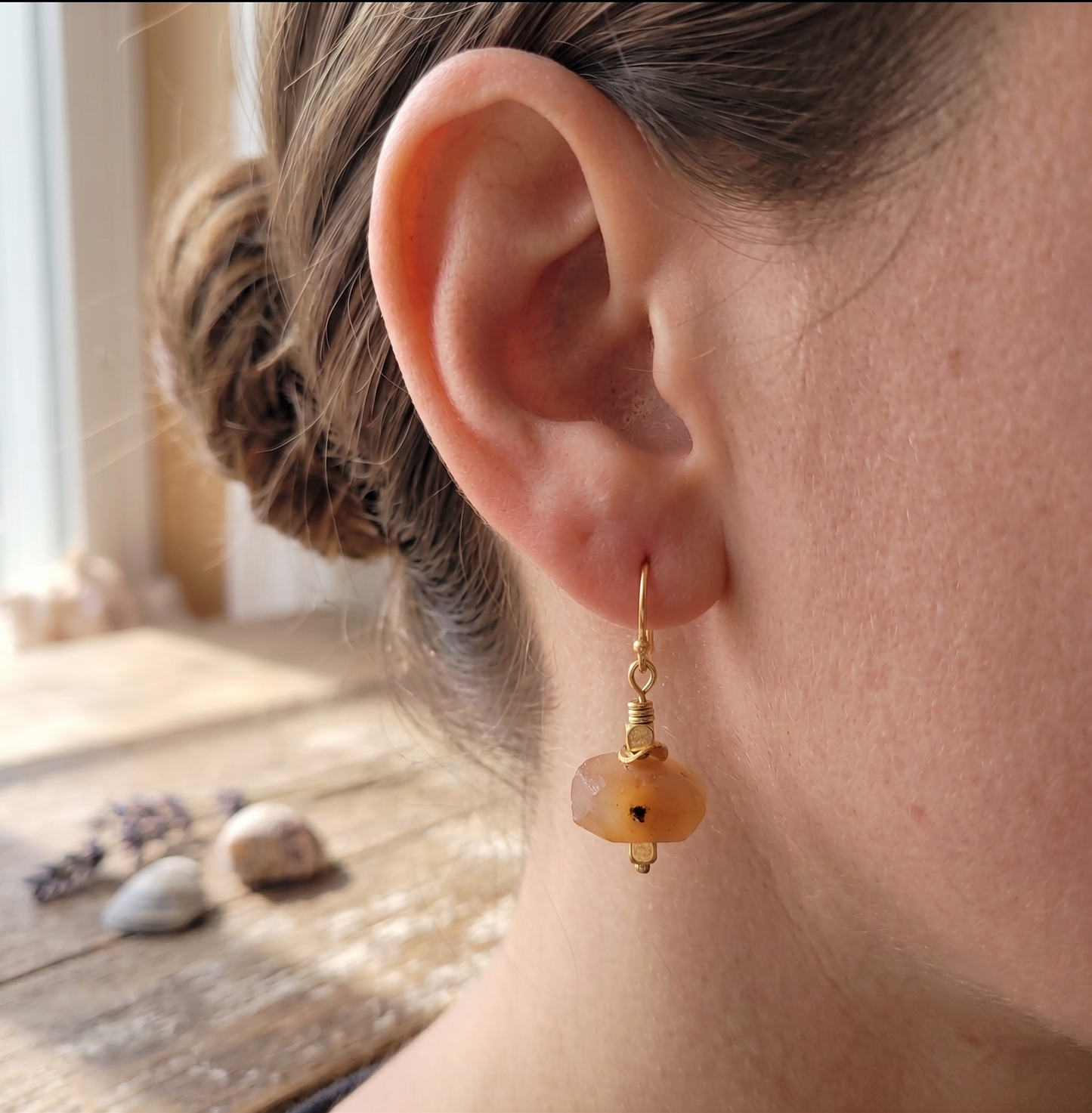 Side view of a woman wearing a faceted orange agate nugget dangle earring with gold-plated accents on a classic French wire hook.