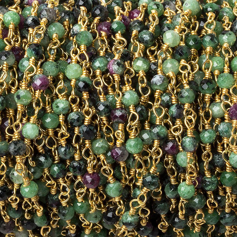 A close-up view of a spool of gold-plated wire-wrapped chain featuring micro-faceted green and purple ruby in zoisite rondelle beads.
