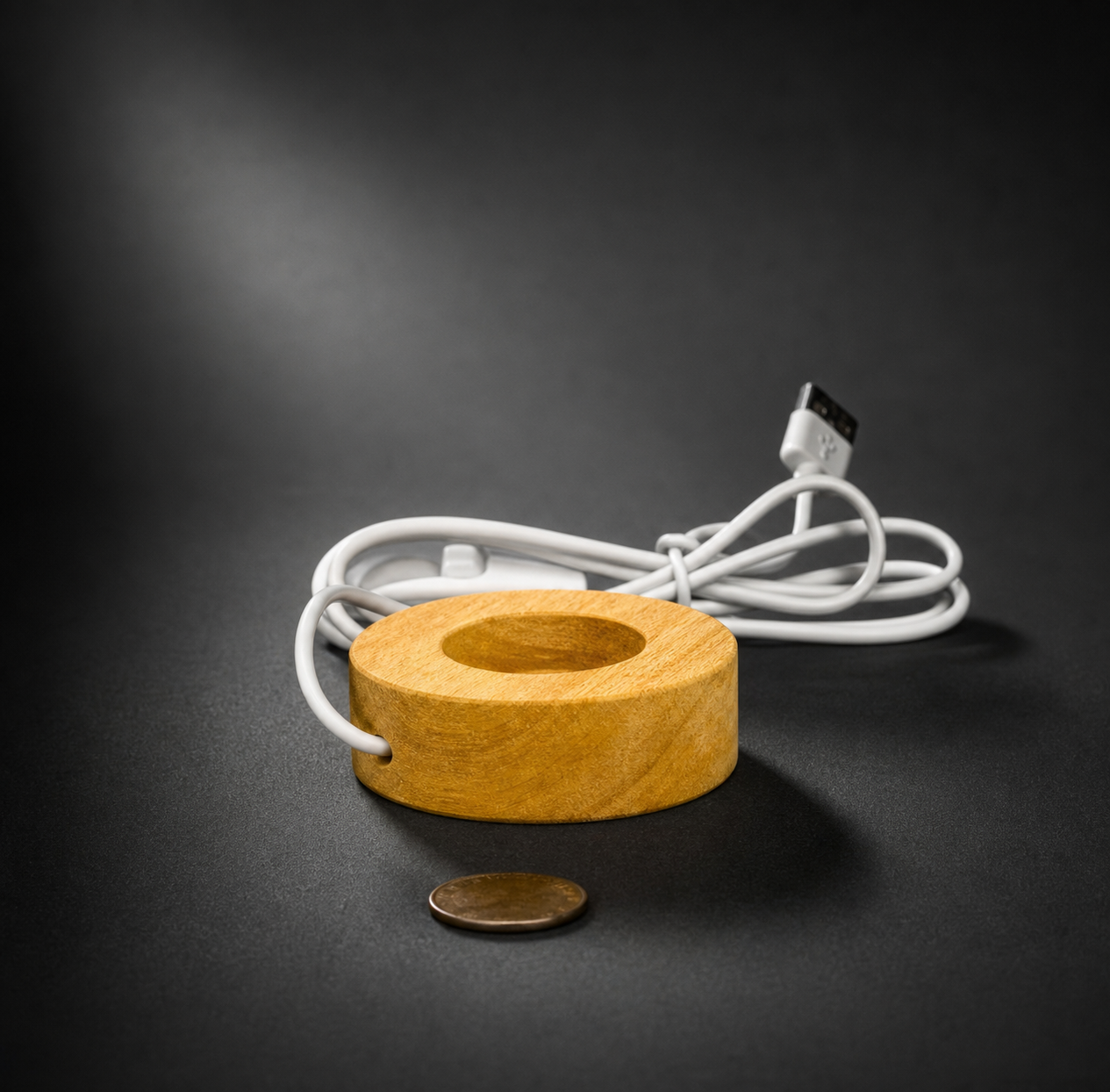 A small round natural wood LED crystal light display base shown from a front angle with an attached white USB power cord and a coin in front for size comparison.